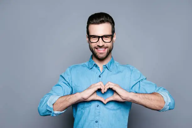 Photo of Portrait of happy handsome man in glasses making heart with fingers