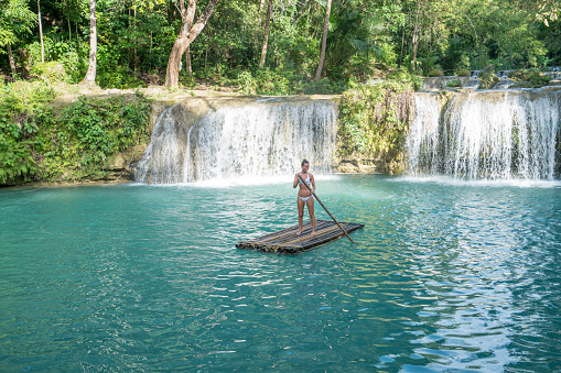 Young woman bamboo rafting on a beautiful waterfall on Siquijor Island in the Philippines. People travel nature outdoor activities concept. One person only enjoying outdoors and tranquillity in a peaceful environment, solo traveler concept