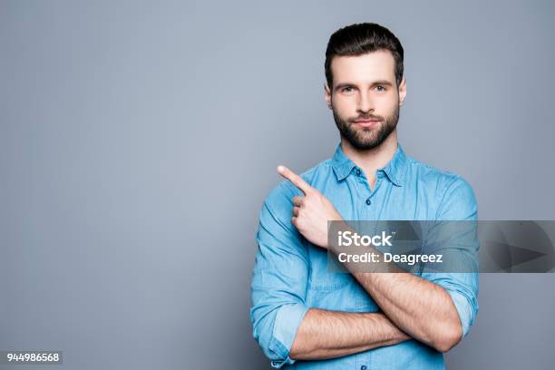 Foto de Sorriso Bonito Barbudo Homem Apontando Para Fora Em Fundo Cinza e mais fotos de stock de Homens