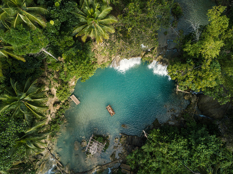 High angle view from drone shot aerial view of young woman bamboo rafting on a beautiful waterfall on Siquijor Island in the Philippines. People travel nature outdoor activities concept. One person only enjoying outdoors and tranquillity in a peaceful environment, solo traveler concept