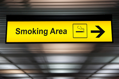 smoking area sign with icon and arrow pointing to smoking area zone hanging from airport ceiling at international terminal. designated smoking areas for separate the smokers from the non-smoking zone
