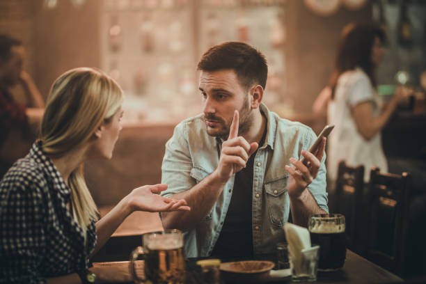 No, I will not show you the text message I have received! Young man using cell phone in a bar and arguing with his girlfriend. friends in bar with phones stock pictures, royalty-free photos & images