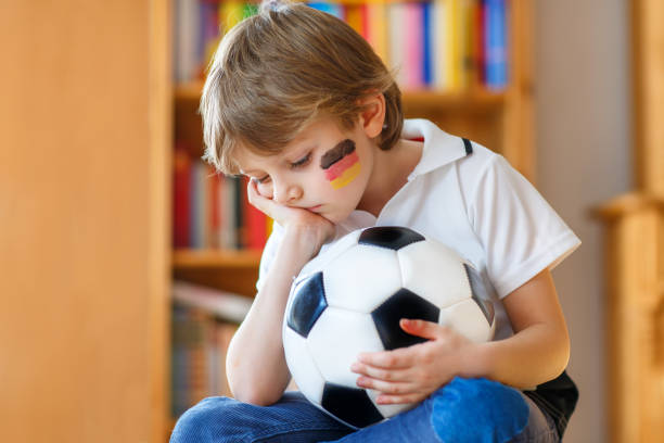 грустный и не счастливый маленький ребенок с футболом о потерянном футболе или футбольном матче. ребенка после просмотра матча по телевизо - youth league стоковые фото и изображения