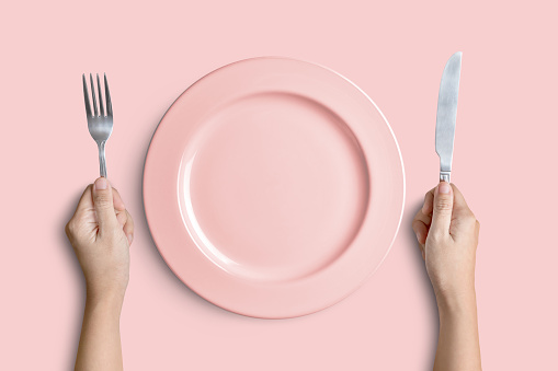 Dinner place setting. A pink plate with silver fork and knife isolated on pink background with clipping path