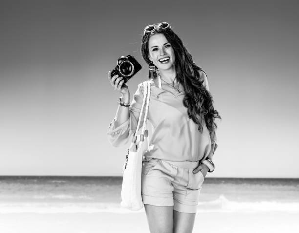 smiling active woman on seacoast showing digital SLR camera