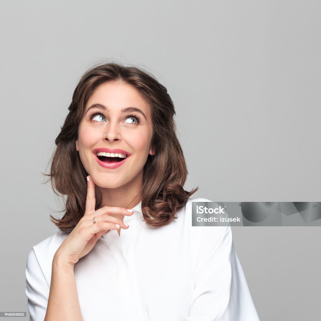 Portrait of happy beautiful young businesswoman Portrait of happy, beautiful young businesswoman looking up with hand on chin against grey background. Looking Up Stock Photo