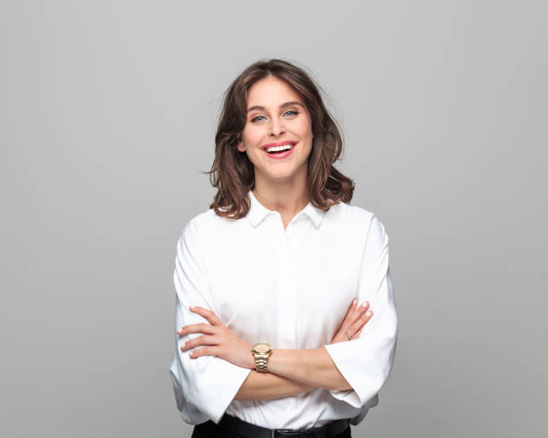 Portrait of beautiful young businesswoman Portrait of confident young businesswoman standing with hand crossed and smiling against grey background. white people stock pictures, royalty-free photos & images