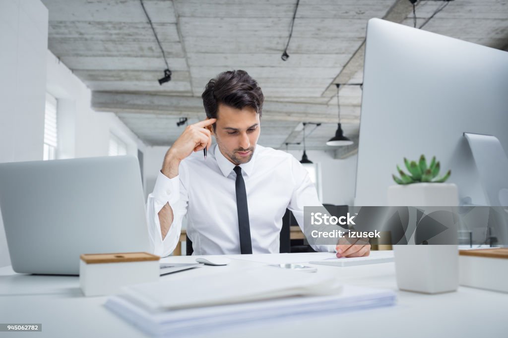Young businessman working in office Young caucasian businessman working in office. Male executive sitting at his desk and reading documnents. 25-29 Years Stock Photo