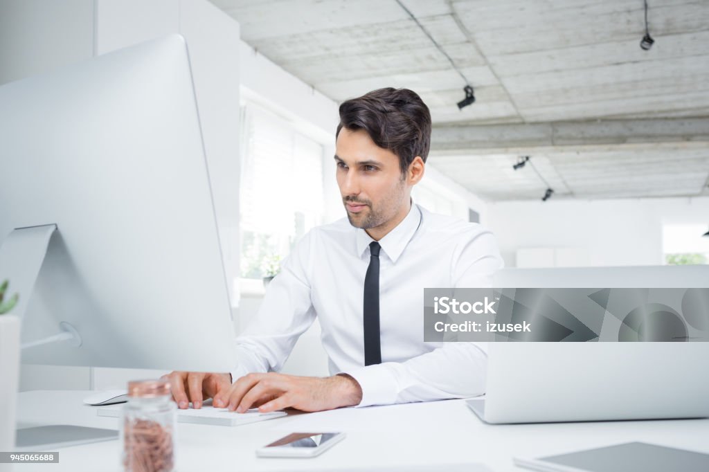 Young businessman working on computer in office Young caucasian businessman working in office. Male executive sitting at his desk and using computer. Financial Advisor Stock Photo