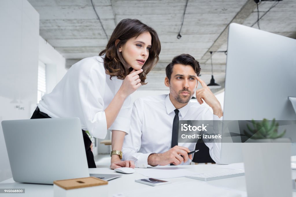 Two business partners working together in office Happy business people working together on laptop. Businessman and businesswoman looking at laptop and smiling in office. 20-29 Years Stock Photo