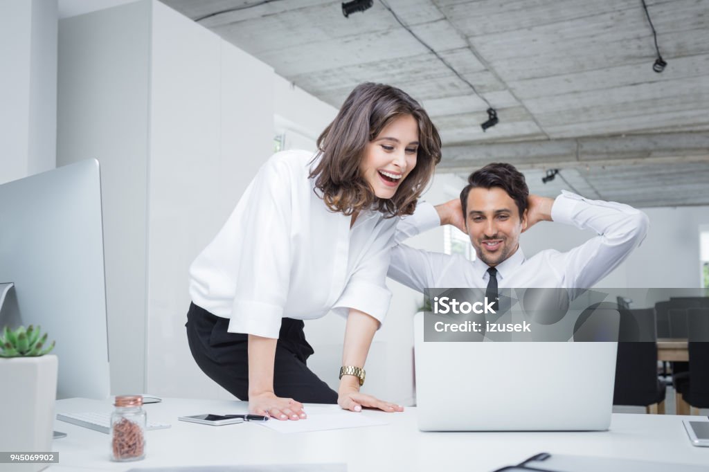 Two business partners working together in office Happy business people working together on laptop. Businessman and businesswoman looking at laptop and celebrating success. 20-29 Years Stock Photo