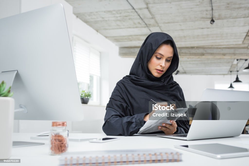 Muslim business woman working in office Business woman working on her laptop in the office. Muslim female in head scarf sitting at her desk using laptop computer. Arabia Stock Photo