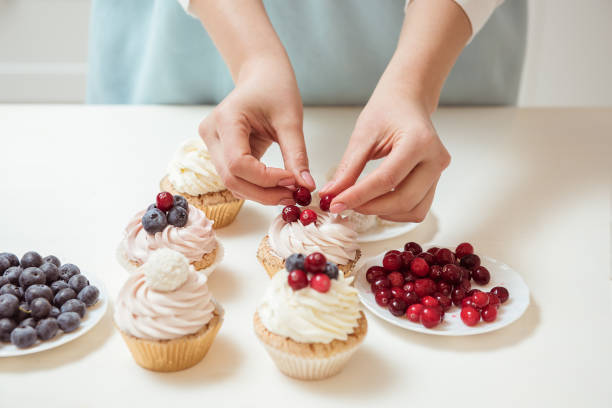 istock Closeup hands of chef decorating cupcakes with colored berries 945074194