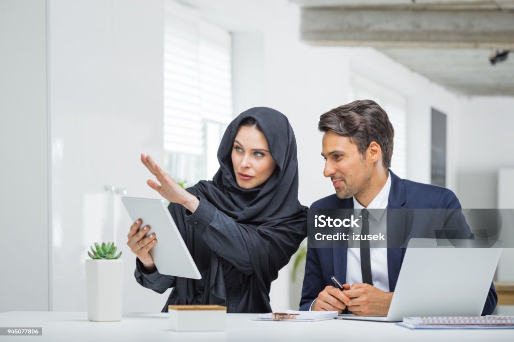 Business couple working together on project at startup office Business couple working together on project at startup office. Musilm businesswoman in hijab with male colleague looking at digital tablet. Business Meeting Stock Photo