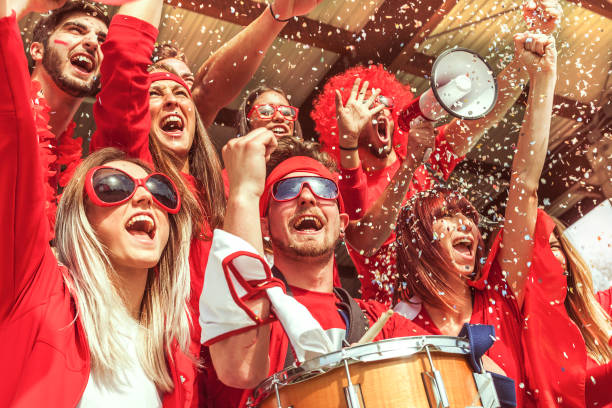 group of fans dressed in red color watching a sports event - women standing fist success imagens e fotografias de stock