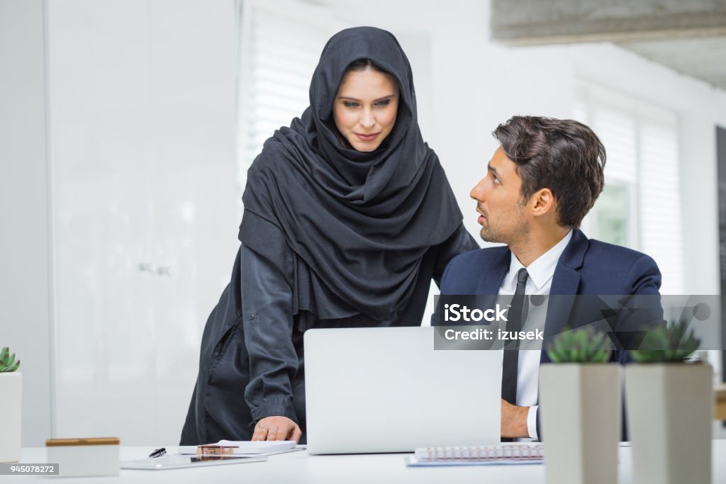 Businessman and muslim businesswoman working together in office Business couple working together on project at startup office. Muslim businesswoman in hijab with male colleague looking at laptop and discussing. Business Stock Photo Businessman and muslim businesswoman working together in office Business couple working together on project at startup office. Muslim businesswoman in hijab with male colleague looking at laptop and discussing. Business Stock Photo