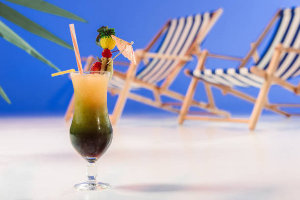 istock Glass with tropical cocktail by deck chairs on blue background 945078406
