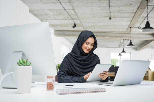 Muslim business woman working in office Smiling business woman working on her laptop in the office. Muslim female in head scarf sitting at her desk using digital tablet and laptop computer. arab woman stock pictures, royalty-free photos & images