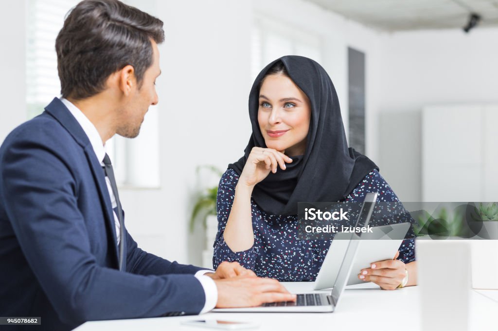 Muslim businesswoman in discussion with colleague Muslim businesswoman holding digital tablet and discussing work with businessman in office. Businesspeople discussing new project. 20-29 Years Stock Photo