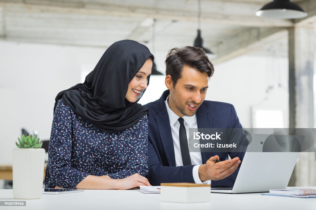 Muslim businesswoman in discussion with colleague Muslim businesswoman discussing work with businessman in office. Businesspeople discussing new project. Office Stock Photo