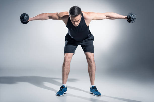 istock Attractive man athlete lifting dumbbells on grey background 945079250