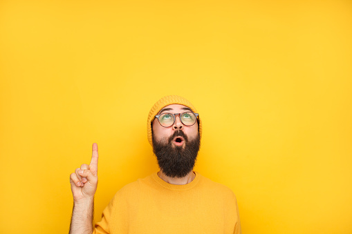 Bright man in yellow sweater and hat looking up and pointing with finger in excitement.