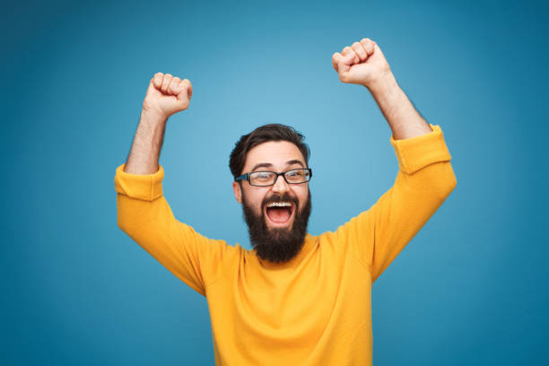 Excited man in yellow holding hands up Young bearded man in eyeglasses and yellow shirt holding hands up in feeling of triumph. arms raised photos stock pictures, royalty-free photos & images