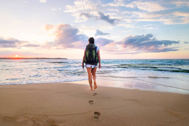 istock Woman with backpack walk on the ocean sand beach at sunset time 945101350