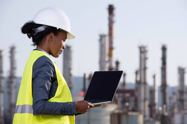 Energy engineer working at refineries checking data. Side view of energy engineer woman wearing work helmet and reflective vest, checking data of the refineries, using a tablet computer. smart grid stock pictures, royalty-free photos & images