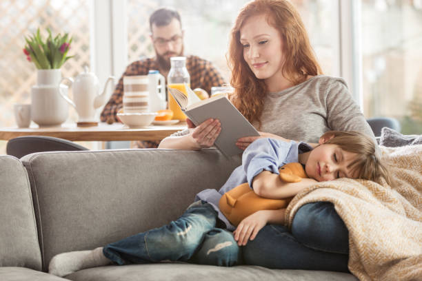 Son lying on mother's laps Sleeping son lying on mother's laps while she is reading a book and father eating in the background mom sleeping on couch stock pictures, royalty-free photos & images