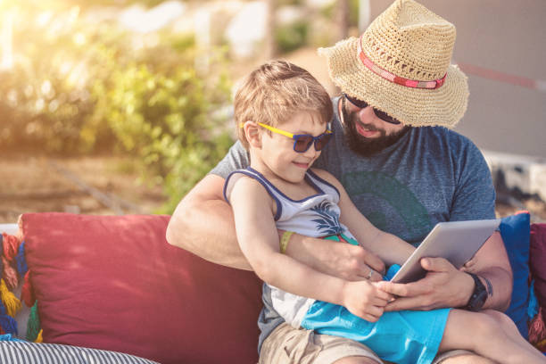 отец и сын на закате с цифровым планшетом в отпуске - child beach digital tablet outdoors стоковые фото и изображения