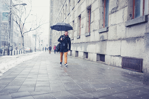 Ginger businessman walking in the snow, under the umbrella. Belgrade, Serbia, Europe