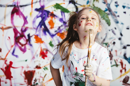 Young child painter standing with a brush in front of a messy background. Creativity.