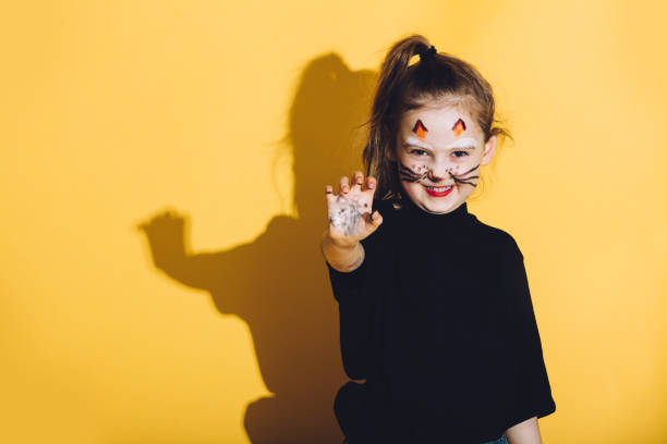 Young girl with cat makeup on her face. Young girl with cat makeup on her face making funny faces. Body painting. Yellow background. cat face paint stock pictures, royalty-free photos & images