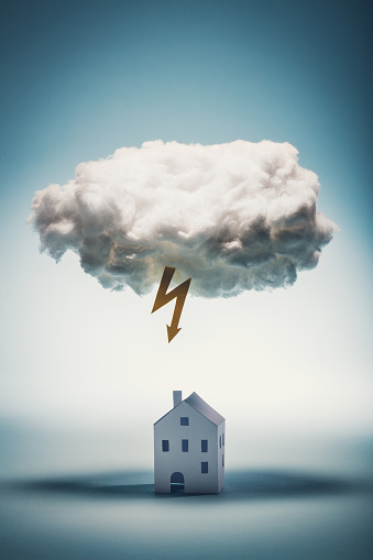 Paper house standing under a white cloud with yellow lightning. Natural distasters. Insurance concept.