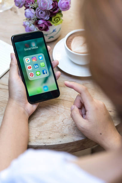 CHIANG MAI, THAILAND - NOVEMBER 14th, 2016: Woman hands using Iphone7 Plus jet black color with icons of social media on screen in coffee shop with latte art, smartphone life style, smartphone era, smartphone in everyday life stock photo