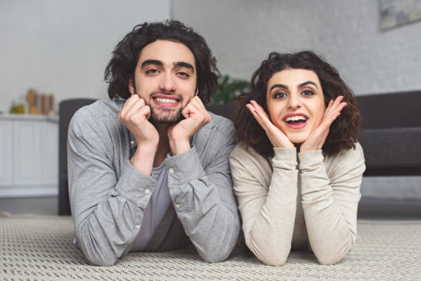 istock happy young couple lying on floor and looking at camera at home 945143888