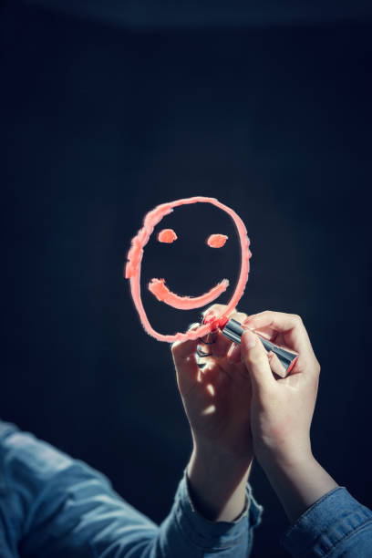 Woman drawing smiley face on a mirror Woman drawing a smiley face on a mirror with a red lipstick. Happiness concept. mirror writing stock pictures, royalty-free photos & images