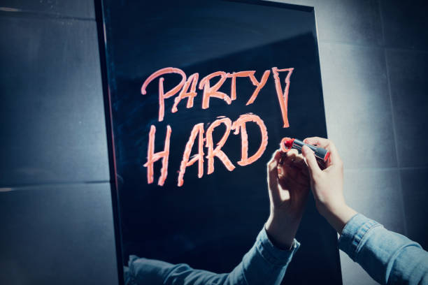 Woman writing "party hard" on a mirror with red lipstick. Woman writing "party hard" on a mirror with red lipstick. Carefree youth. Clubbing and partying. mirror writing stock pictures, royalty-free photos & images