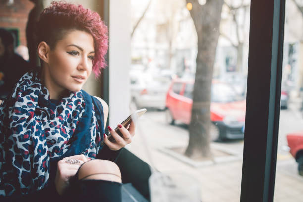 Short haired girl in cafe An attractive short haired girl sitting by a window in a cafe holding a smartphone looking out half shaved hairstyle stock pictures, royalty-free photos & images