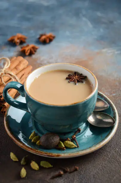 Photo of Indian masala chai tea. Spiced tea with milk on dark rusty background.