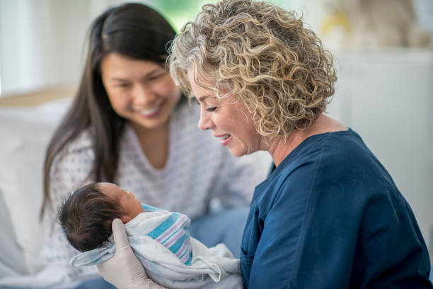 The nurse and mother look and smile at the newborn baby who is lying in the nurse's hands