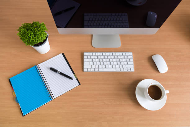 istock All in one computer, mouse, keyboard, phone, note book, coffee cup and tree vase  on wooden table 945192022