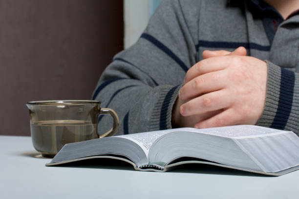 istock A young man reads the Bible with a silver slice sitting at the table. A mug with water is next to it. 945200058