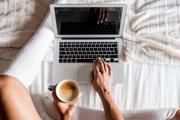 istock woman smiling drinking a coffee and working with her computer on bed 945200314