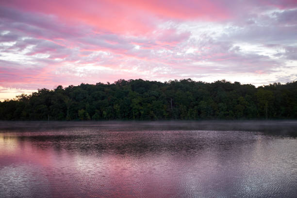 Spectacular pink sunset reflected in a tranquil lake with surrounding vegetation on low hills in a scenic landscape
