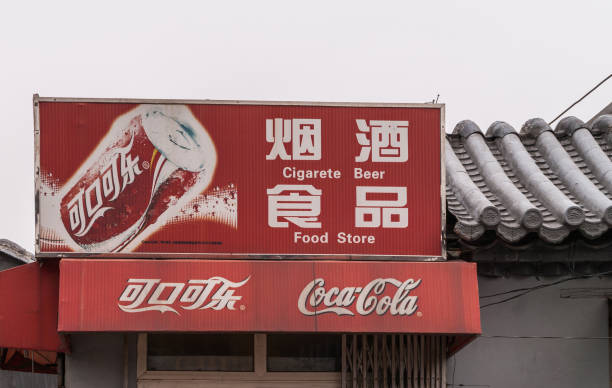 Red Coca-Cola sign with spelling error in Beijing, China. Beijing, China - April 26, 2010: Closeup of red Coca-Cola sign fixed on gray roof against silver sky. Read in English and Mandarin about beer, cigarette and food. misspelled stock pictures, royalty-free photos & images