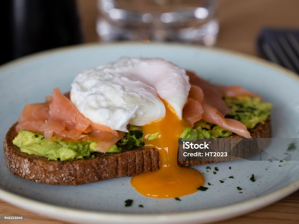 Bread with avocado, smoked salmon and poached egg yolk flowing Rye Bread with smashed avocado, smoked salmon and poached egg with yolk flow Animal Egg Stock Photo