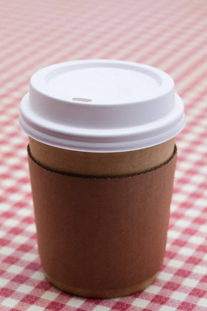 istock Cardboard throwaway coffee cup on red and white checkered table 945264386