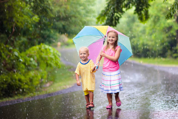 istock Kid with umbrella playing in summer rain. 945289848